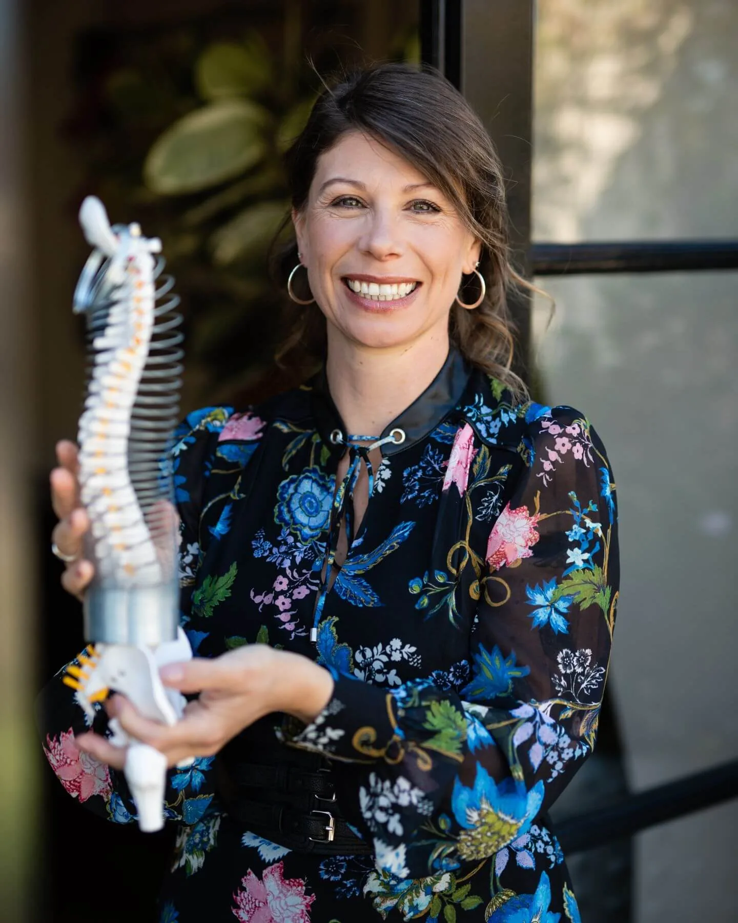 Carolyn Hitchcock, a specialist Soft Tissue Therapist in London, smiling while holding an anatomical model of the human spine.